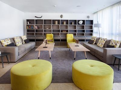 Moderní obývací pokoj se šedými pohovkami, žlutými křesly a kulatým kobercem před knihovnou.