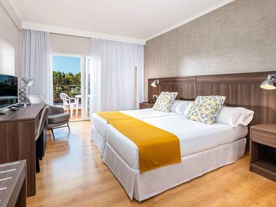 Světý hotelový pokoj s manželskou postelí, psacím stolem a balkonem s výhledem ven.