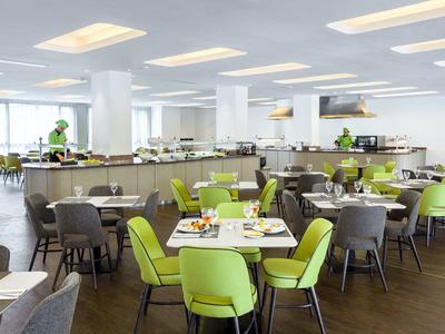 Moderní hotelová jídelna se světle zelenými a šedými židlemi u kulatých stolů a velkou bufetovou částí.