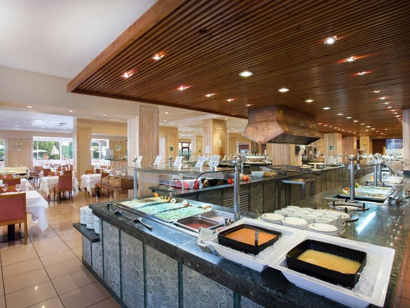 Área de buffet en restaurante de hotel con estaciones de comida y mesas al fondo