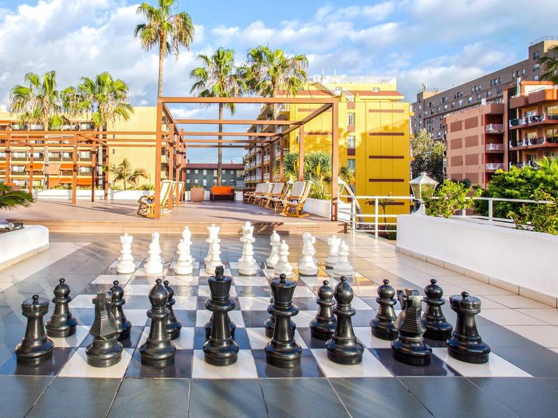 Gran tablero de ajedrez al aire libre en hotel con palmeras y edificio de fondo
