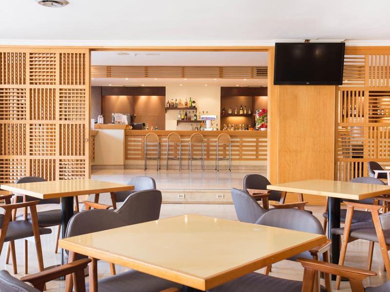 Sala de desayunos moderna con muebles de madera y una barra al fondo en un hotel.