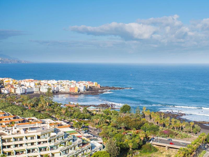 Vista costera con playa, mar y edificios bajo un cielo azul con nubes dispersas.