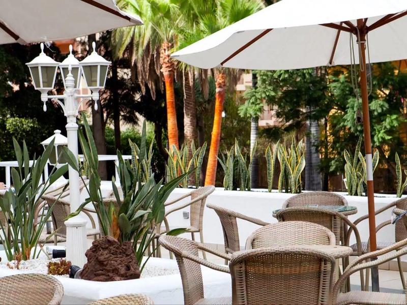 Terraza con sombrillas, sillas de mimbre y mesas en un área exterior verde