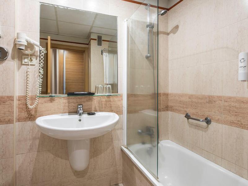 Baño limpio con lavabo, bañera y espejos grandes en tonos beige y marrón.