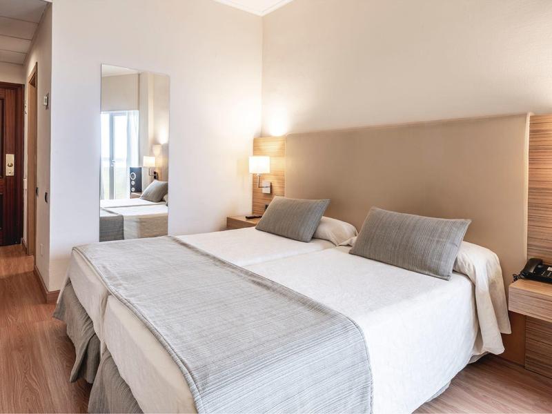 Habitación de hotel luminosa con cama doble, mesas de noche, lámparas y suelo de madera.