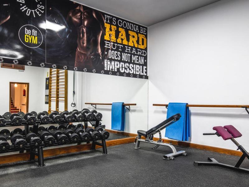Gimnasio moderno con mancuernas, banco de entrenamiento y espejo en una habitación luminosa.