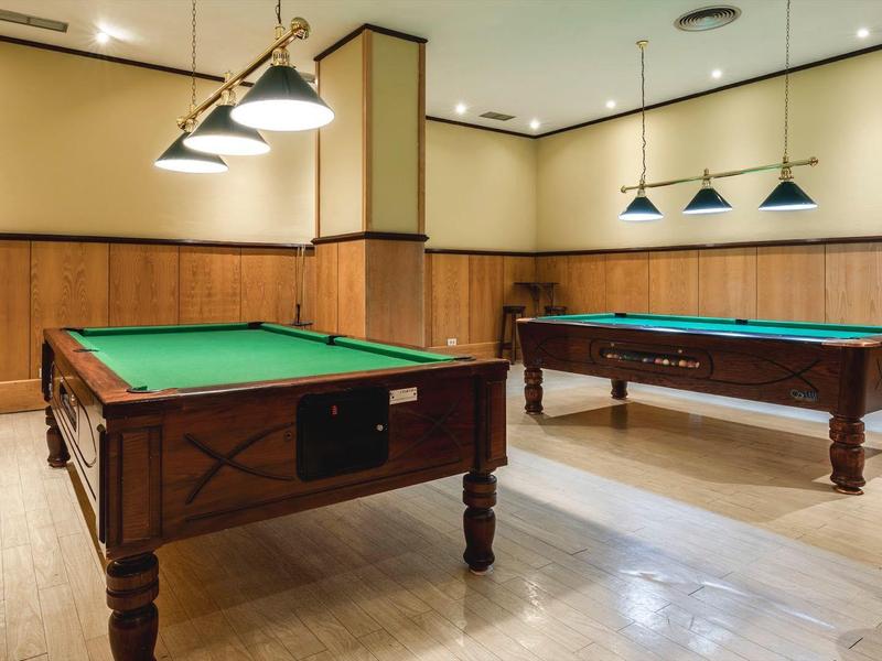Sala bien iluminada con dos mesas de billar y paneles de madera en las paredes.