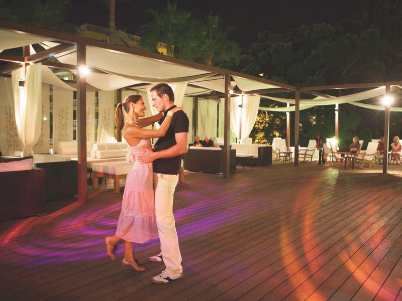 Pareja bailando en una terraza de madera iluminada de un hotel por la noche.