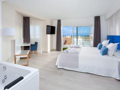 Lichte hotelkamer met tweepersoonsbed, whirlpool, bureau en uitzicht op de stad.