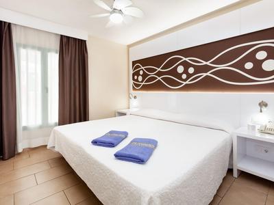 Licht ingerichte slaapkamer met tweepersoonsbed, twee blauwe handdoeken en abstracte wanddecoratie.