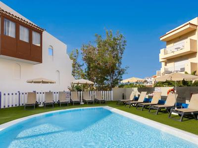 Klein buitenzwembad met ligstoelen en parasols naast een hotelgebouw bij zonnig weer.