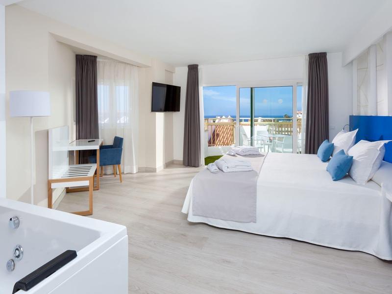 Lichte hotelkamer met tweepersoonsbed, whirlpool, bureau en uitzicht op de stad.