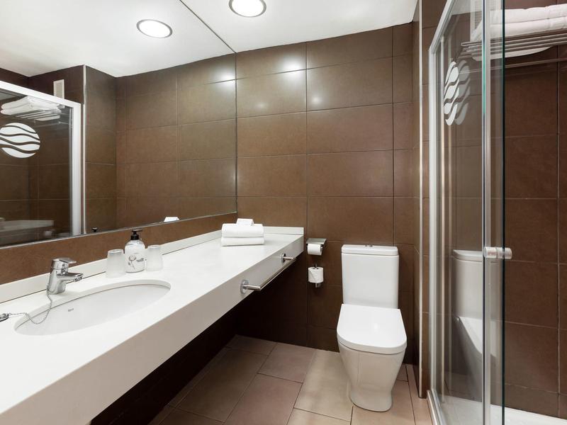 Moderne badkamer met bruine tegels, witte wastafel, toilet en douchecabine.