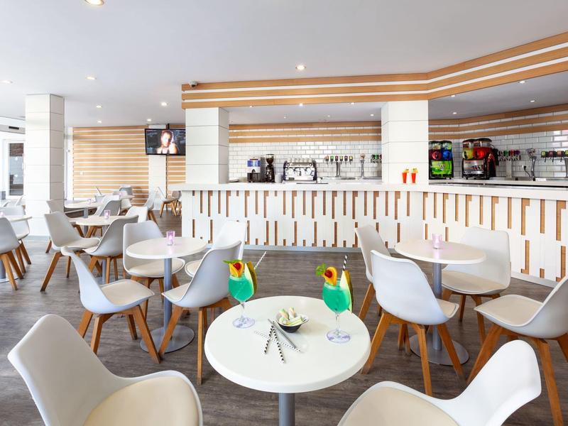 Licht ontbijtruimte met ronde witte tafels en lichtgrijze stoelen.