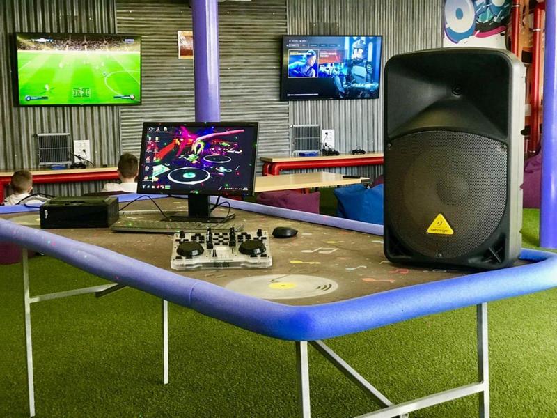 Een tafel met DJ-apparatuur en luidspreker in een kamer met tv's aan de muur.