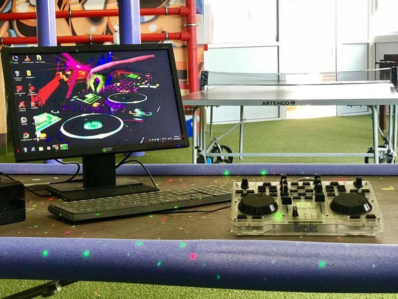 Computer met DJ-software naast een mengpaneel en tafeltennistafel in een kamer met groen tapijt.