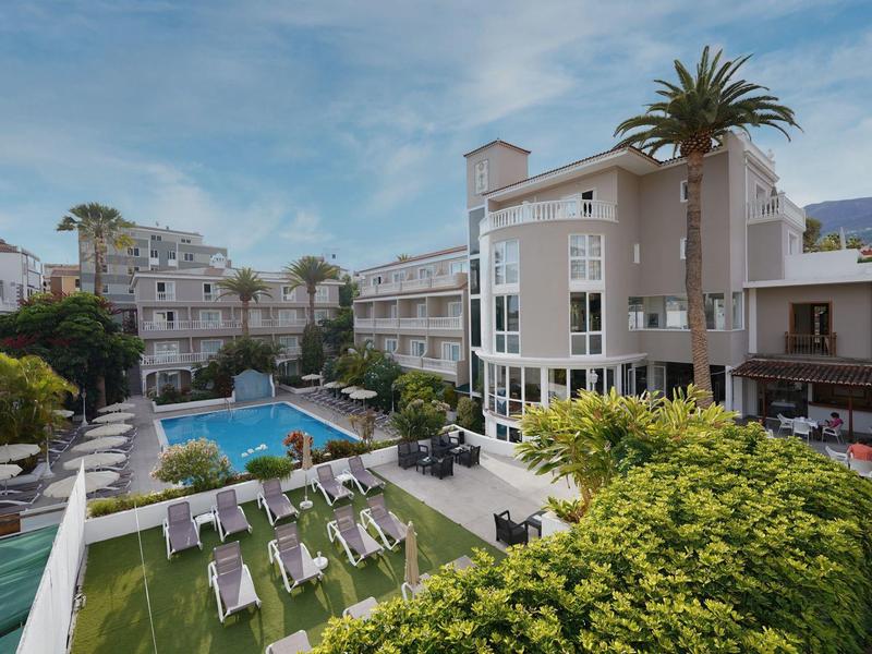 Modern hotel complex with pool, lounge chairs, and lush greenery under blue sky