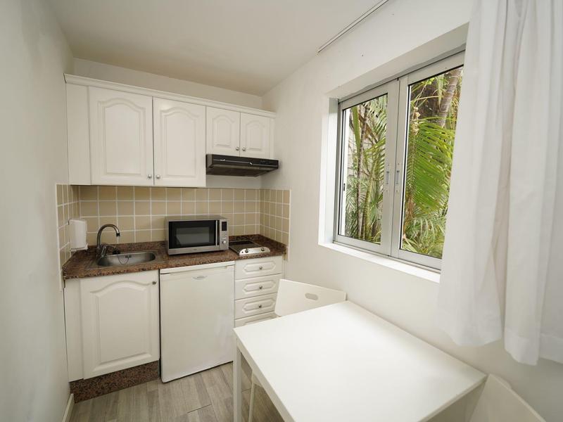 Small kitchenette with white cabinets, microwave, mini fridge, and table next to window overlooking plants