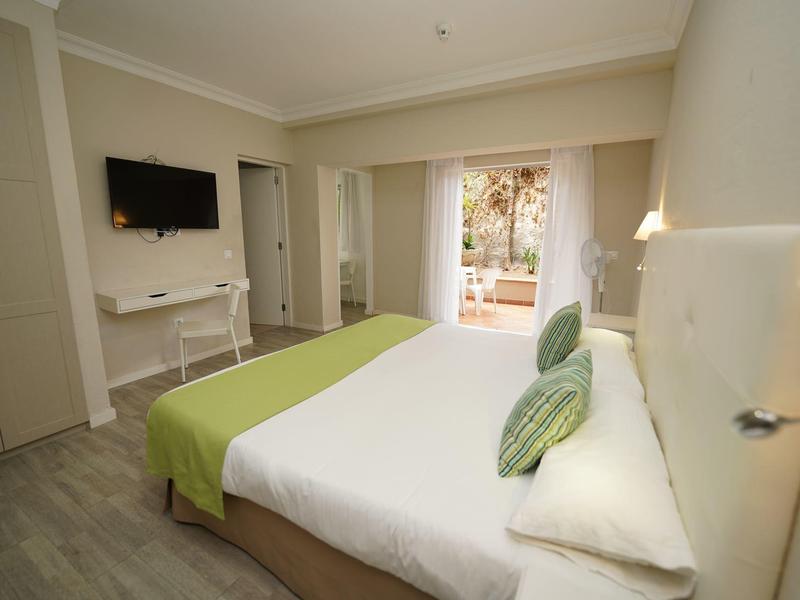 Modern hotel room with double bed, wall-mounted TV, and access to a terrace.