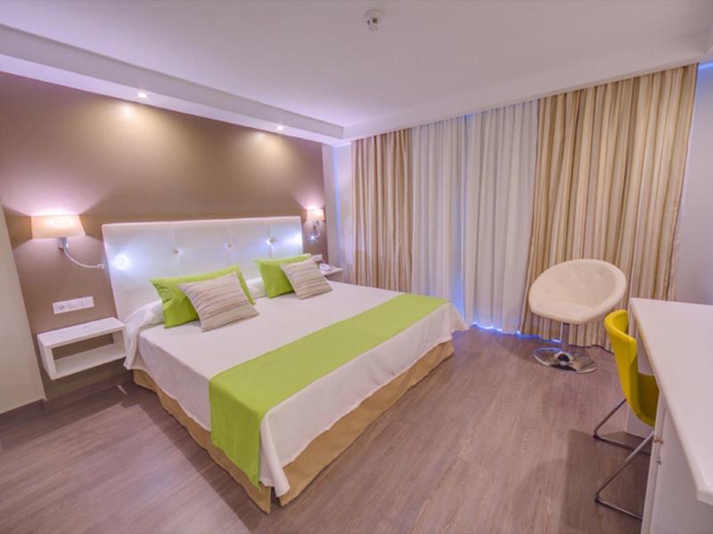 Modern hotel room with large bed, green accents, and desk area