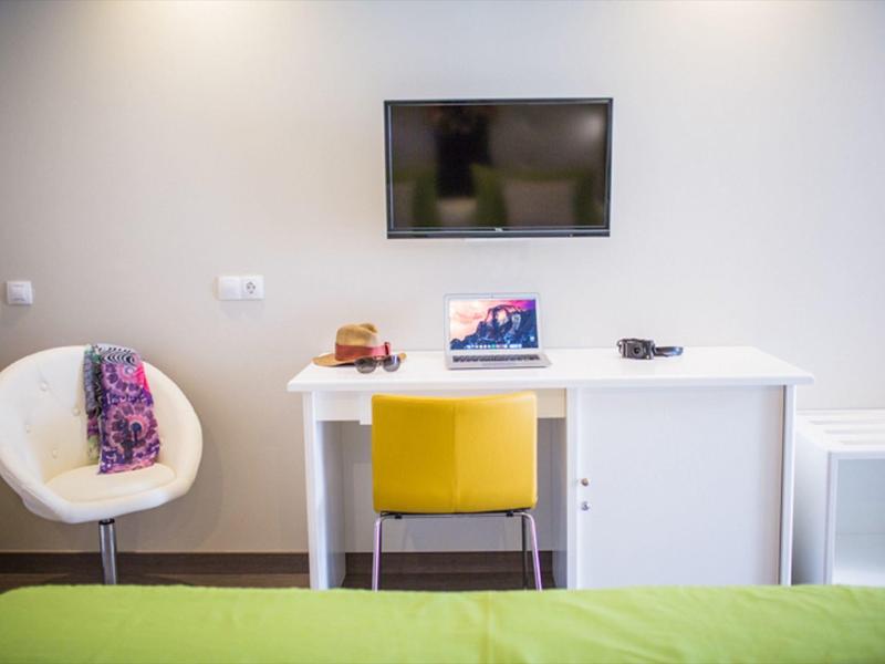 Modern hotel room workspace with a white desk, yellow chair, and wall-mounted TV.