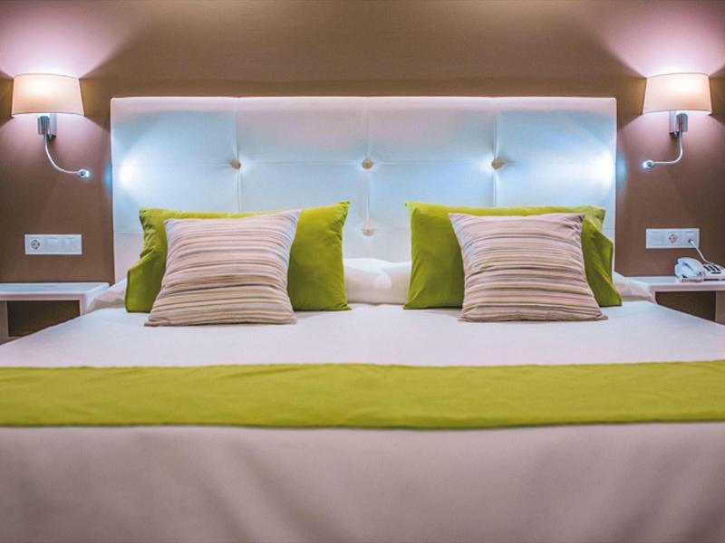 Modern hotel room with bed, blue padded headboard, and green accent pillows