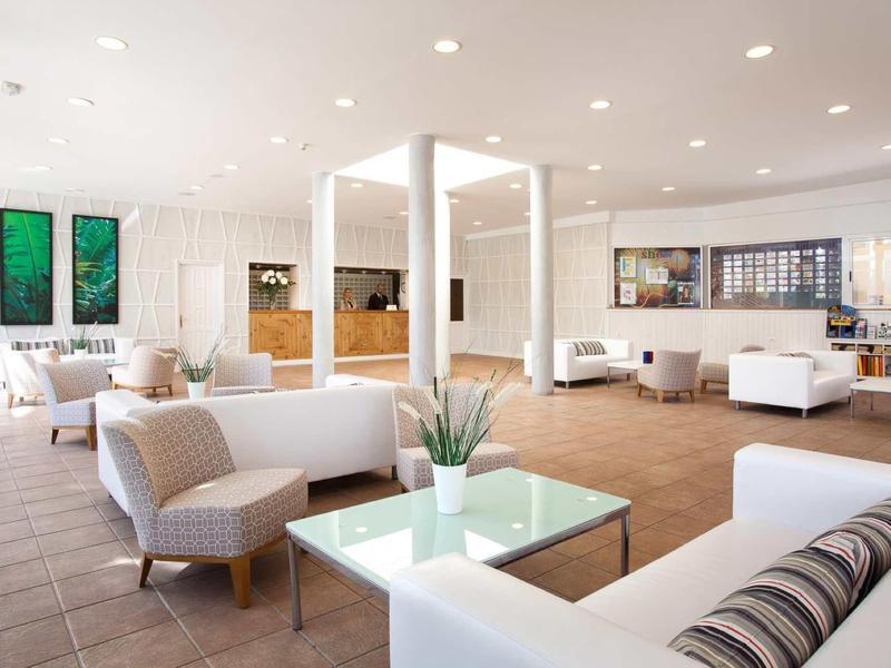 Espace lounge d'hôtel lumineux et moderne avec canapés blancs et beiges, fauteuils et tables carrées.