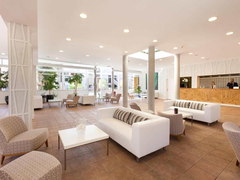 Espace lounge d'hôtel lumineux et moderne avec canapés blancs, fauteuils et comptoir en bois.