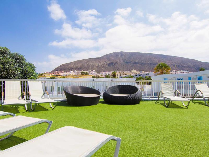 Terrasse avec transats et fauteuils ronds offrant une vue sur les collines et le ciel bleu
