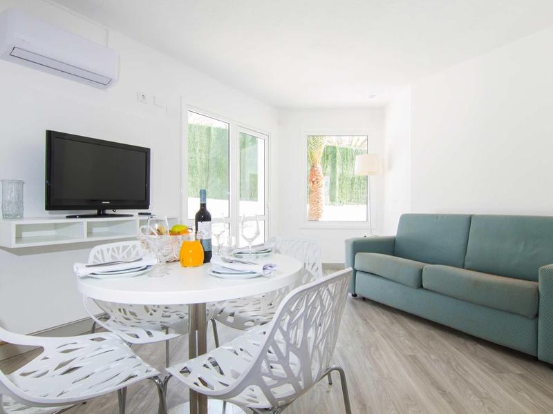 Salon lumineux avec table à manger, télévision à écran plat et canapé vert.