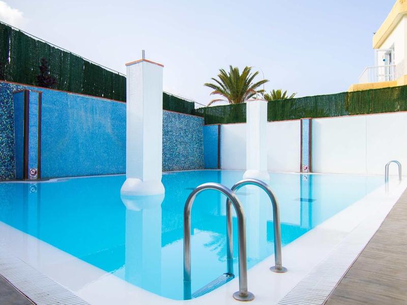 Piscine extérieure moderne avec mur carrelé bleu et haie de jardin dans un hôtel.