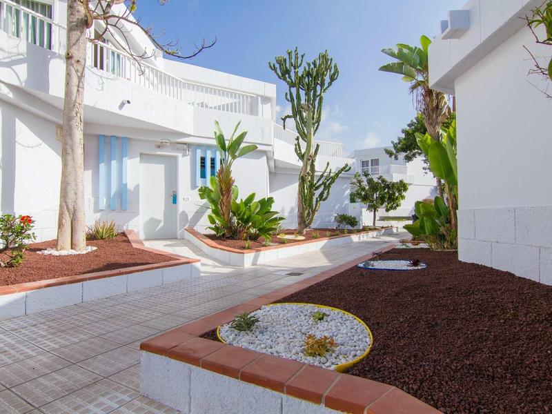 Espace extérieur moderne avec bâtiments blancs, plantes en fleurs et ciel bleu clair.