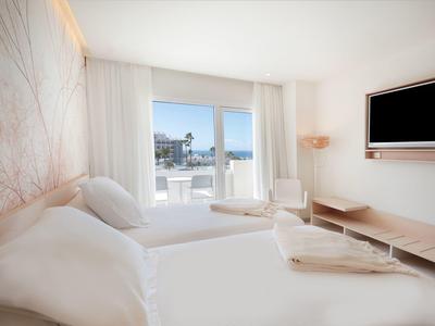 Modern hotelkamer met twee bedden en een balkon met uitzicht op zee.