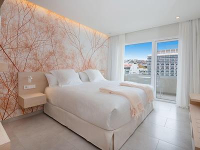 Modern hotelkamer met groot bed, balkon en decoratief wandontwerp.