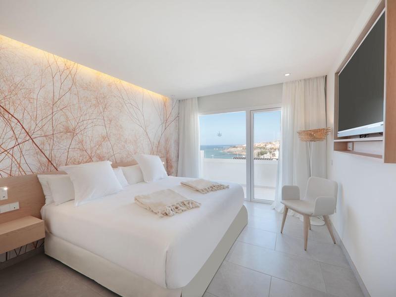 Lichte hotelkamer met tweepersoonsbed, tv, balkon en moderne wanddecoratie.