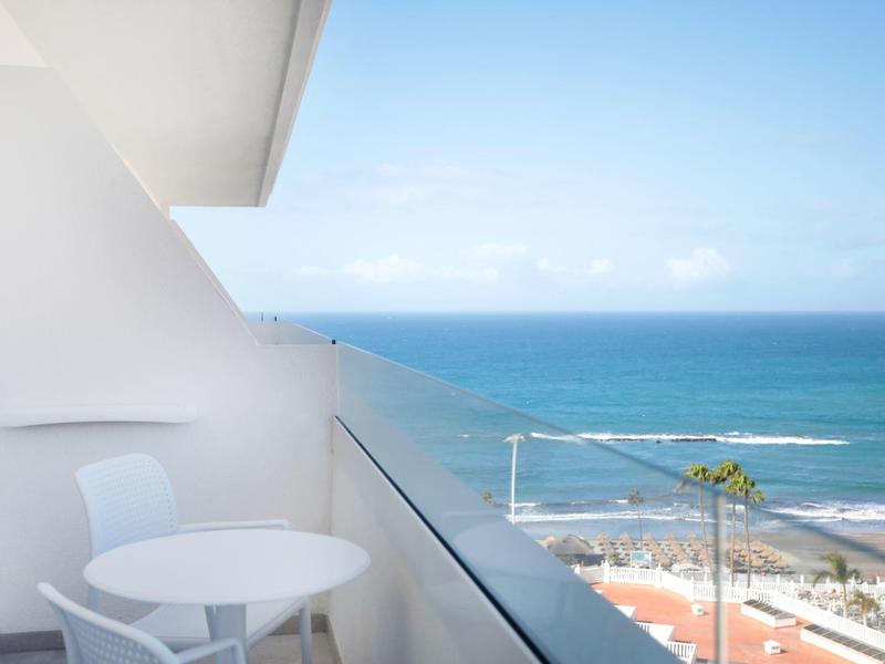 Balkon met witte tafel en stoelen met uitzicht op zee en strand.