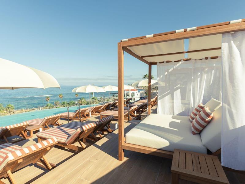 Zonnig terras met ligbed en ligstoelen met uitzicht op zee.