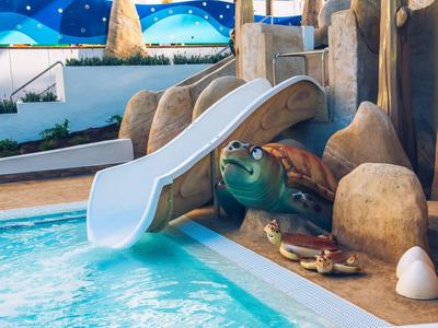 Piscina infantil con tobogán en forma de tortuga y rocas, agua clara y limpia.