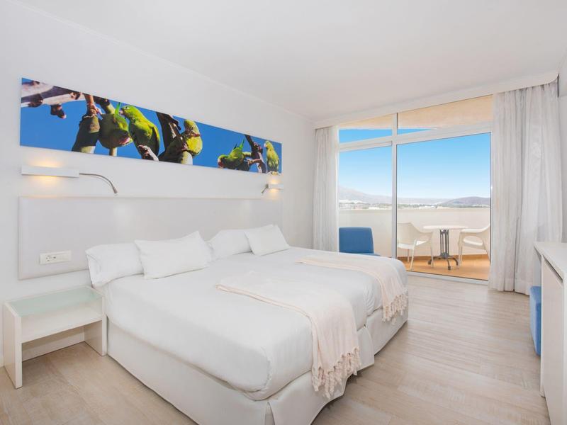 Habitación de hotel luminosa con dos camas individuales, vista al mar y balcón con área de estar.