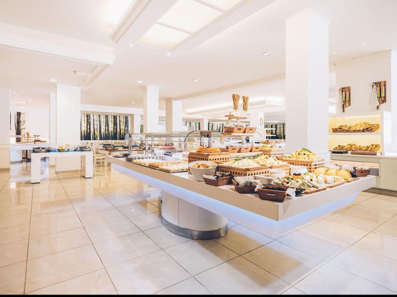 Sala de desayuno luminosa con mesas buffet y variedad de productos de panadería en un hotel.