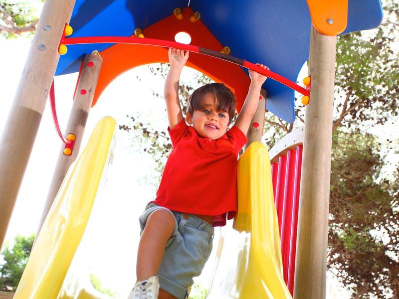 Niño jugando alegremente en un colorido parque infantil bajo el sol.