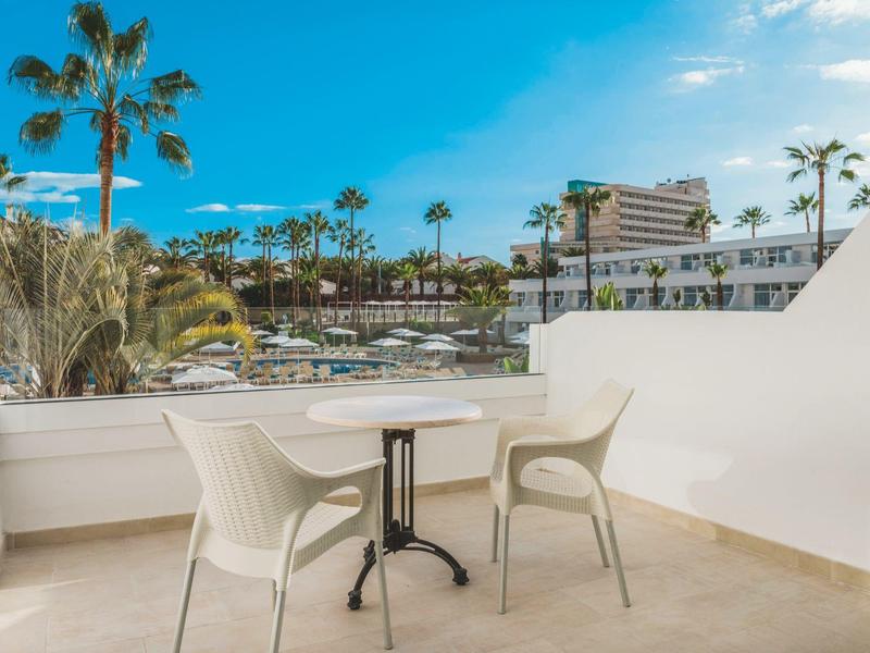 Balcón con mesa y dos sillas con vista a jardín de palmeras y hotel