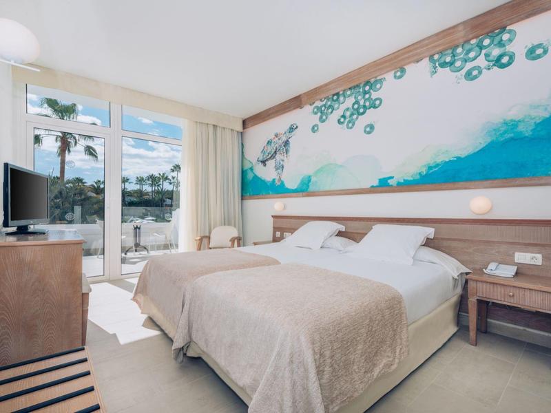 Habitación de hotel luminosa con cama doble, vista al mar y decoración moderna.