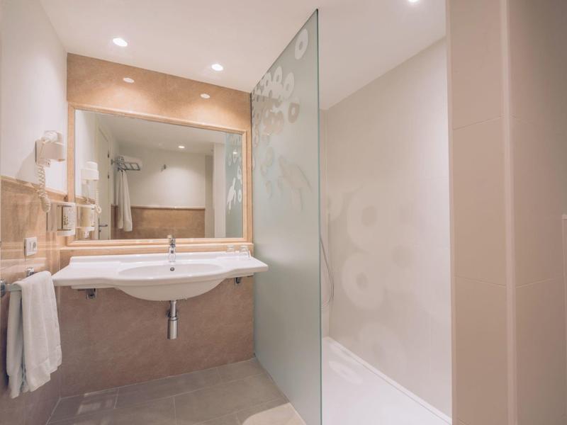 Baño luminoso con espejo grande, lavabo doble y ducha a ras de suelo con mampara de vidrio.