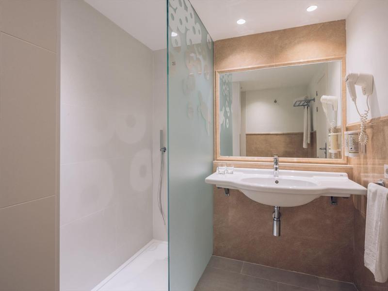 Baño moderno con ducha, lavabo, espejo grande y toallas en la pared.