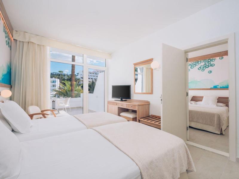 Habitación de hotel luminosa con cama doble, televisión y acceso al balcón.