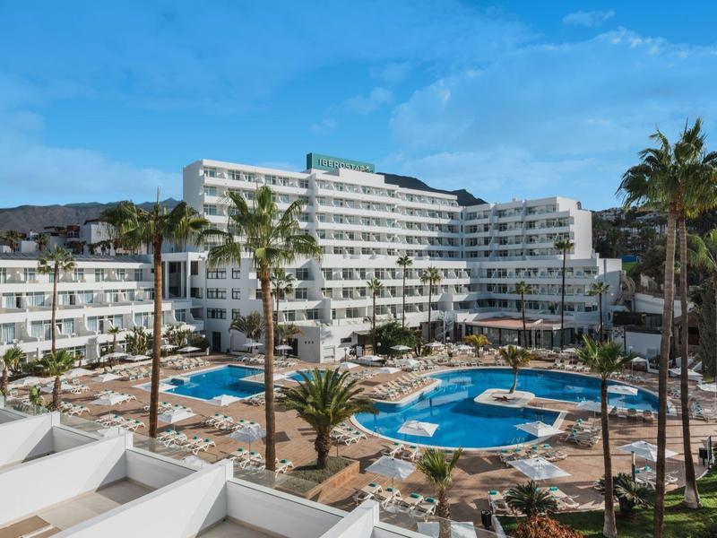 Gran complejo hotelero con varias piscinas y palmeras bajo un cielo azul.