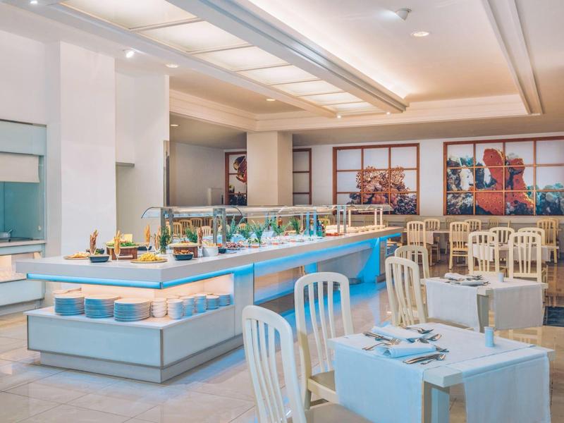 Restaurante de hotel moderno y luminoso con buffet y mesas vestidas en blanco y azul.