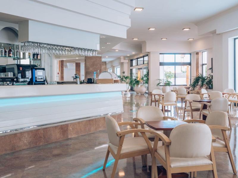 Restaurante moderno y luminoso con mesas de madera y sillas beige, grandes ventanas.